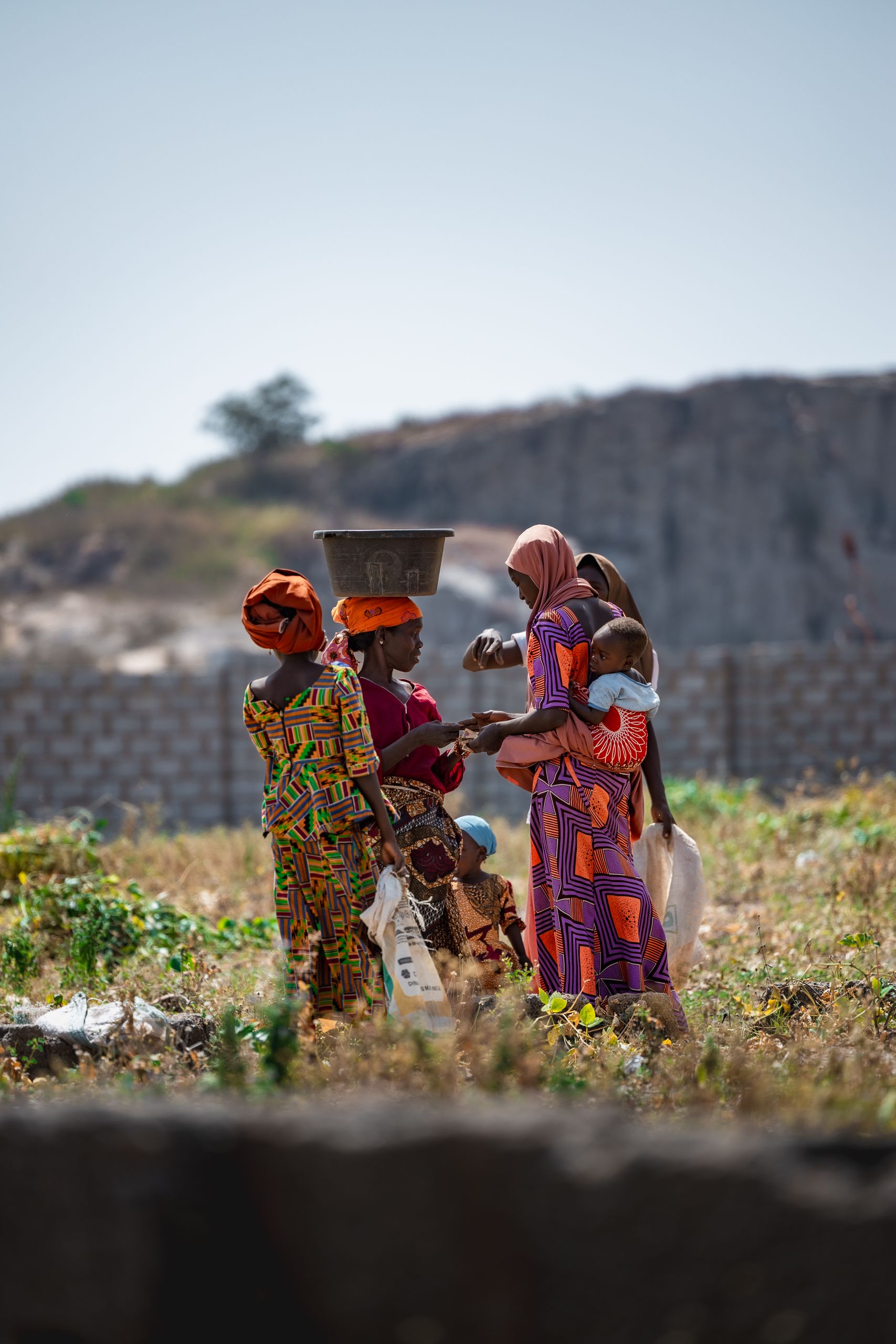 African women in traditional attire interacting outdoors in Deidei, Kaduna, Nigeria.