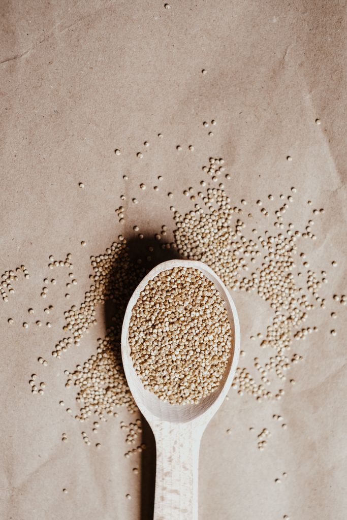 Top view of organic quinoa seeds in a wooden spoon on brown paper.